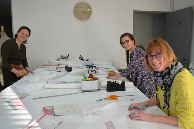 Trois stagiaires en formation de modélisme chez FLK Creations, travaillant ensemble sur un patron de robe.