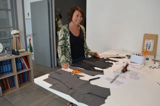 Stagiaire souriante de FLK Créations en formation professionnelle, travaillant sur une table avec des pièces de tissus devant elle.