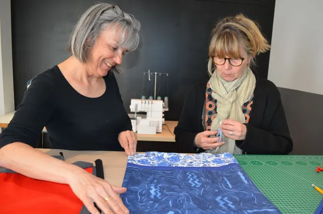 Deux femmes stagiaires de FLK Créations choisissant entre deux tissus lors d&apos;une formation professionnelle en couture.